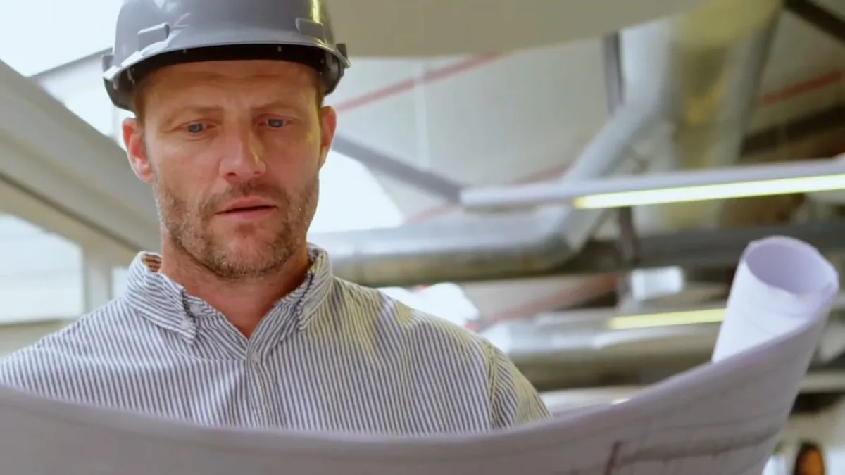 plumber reviewing drawings beneath overhead pipe runs shown as hero overview for Plumbing Services in Glendora, CA